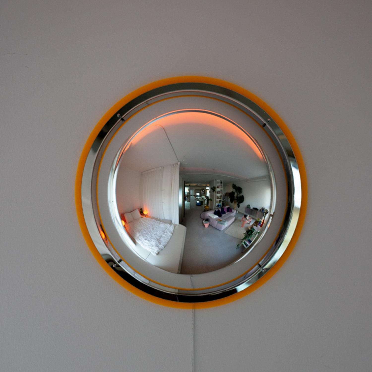 BUBBLE Wandlampe frontal an grauer Wand – orangener LED-Ring mit Wohnraum-Spiegelung