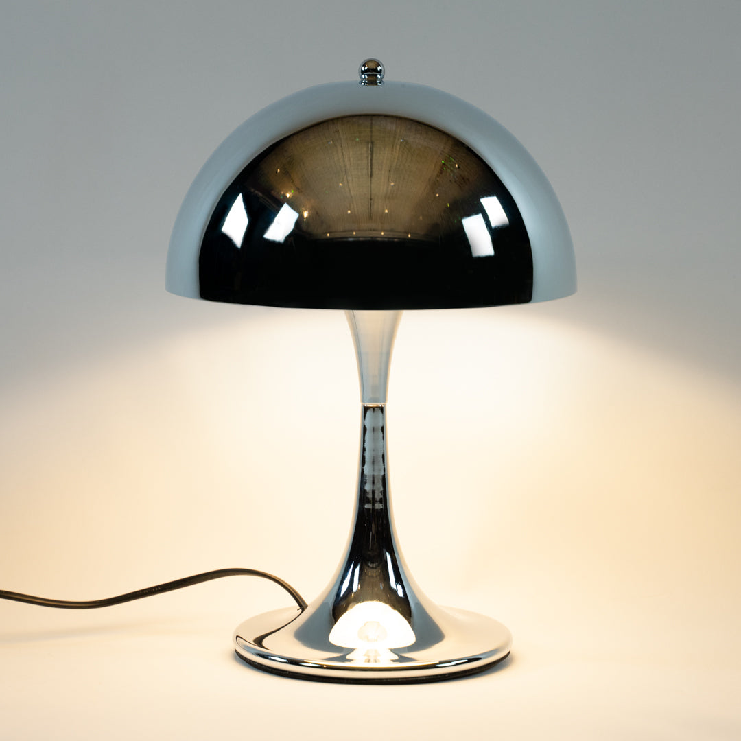 Eine stilvolle Chromlampe im Mid-Century Design, präsentiert auf einem grafischen Würfel im modernen Vintage-Stil. Diese Space Age Tischlampe ist ideal als elegante Nachttischlampe oder für die Wohnzimmereinrichtung im 70er Jahre Look.