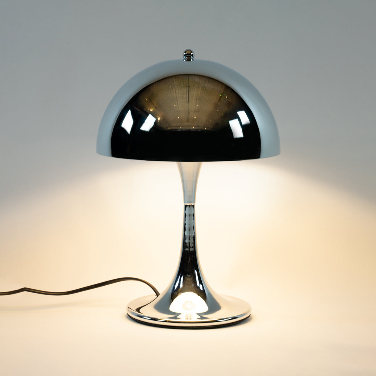 Eine stilvolle Chromlampe im Mid-Century Design, präsentiert auf einem grafischen Würfel im modernen Vintage-Stil. Diese Space Age Tischlampe ist ideal als elegante Nachttischlampe oder für die Wohnzimmereinrichtung im 70er Jahre Look.
