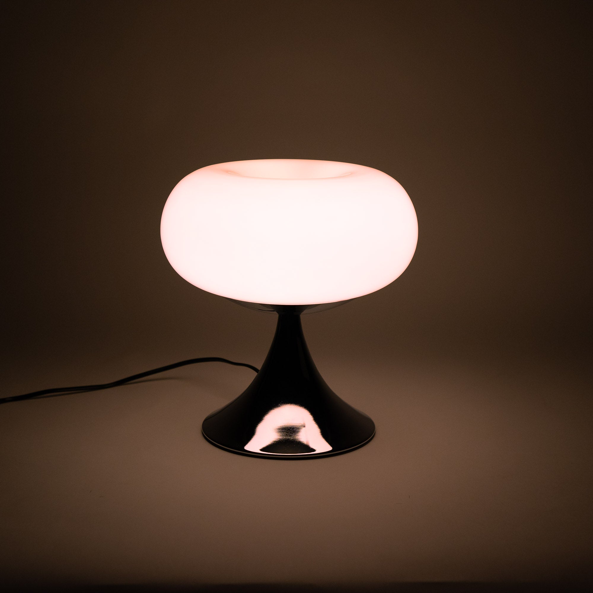 Space Age Tischlampe mit weißem, opalem Glasschirm und glänzendem Chromfuß. Die Lampe strahlt ein weiches, warmes Licht aus und steht auf einem schlichten Untergrund. Retro-inspirierte Mid-Century Beleuchtung, ideal für Schlafzimmer oder Wohnzimmer im minimalistischen Design.
