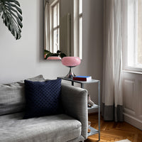 Die sanfte Beleuchtung der Space Age Lampe sorgt für eine warme Atmosphäre. Die Lampe steht auf einem Metall-Beistelltisch neben einem grauen Sofa mit dunkelblauem Kissen. Ein Spiegel reflektiert die Lichtstimmung, Vorhänge lassen weiches Tageslicht herein.