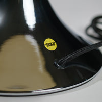 Nahaufnahme der verchromten GLOW UP STUDIO Donut Lampe mit gelbem Markensticker und schwarzem Textilkabel. Der reflektierende Metall Oberfläche zeigt hochwertige Verarbeitung und modernes Design.