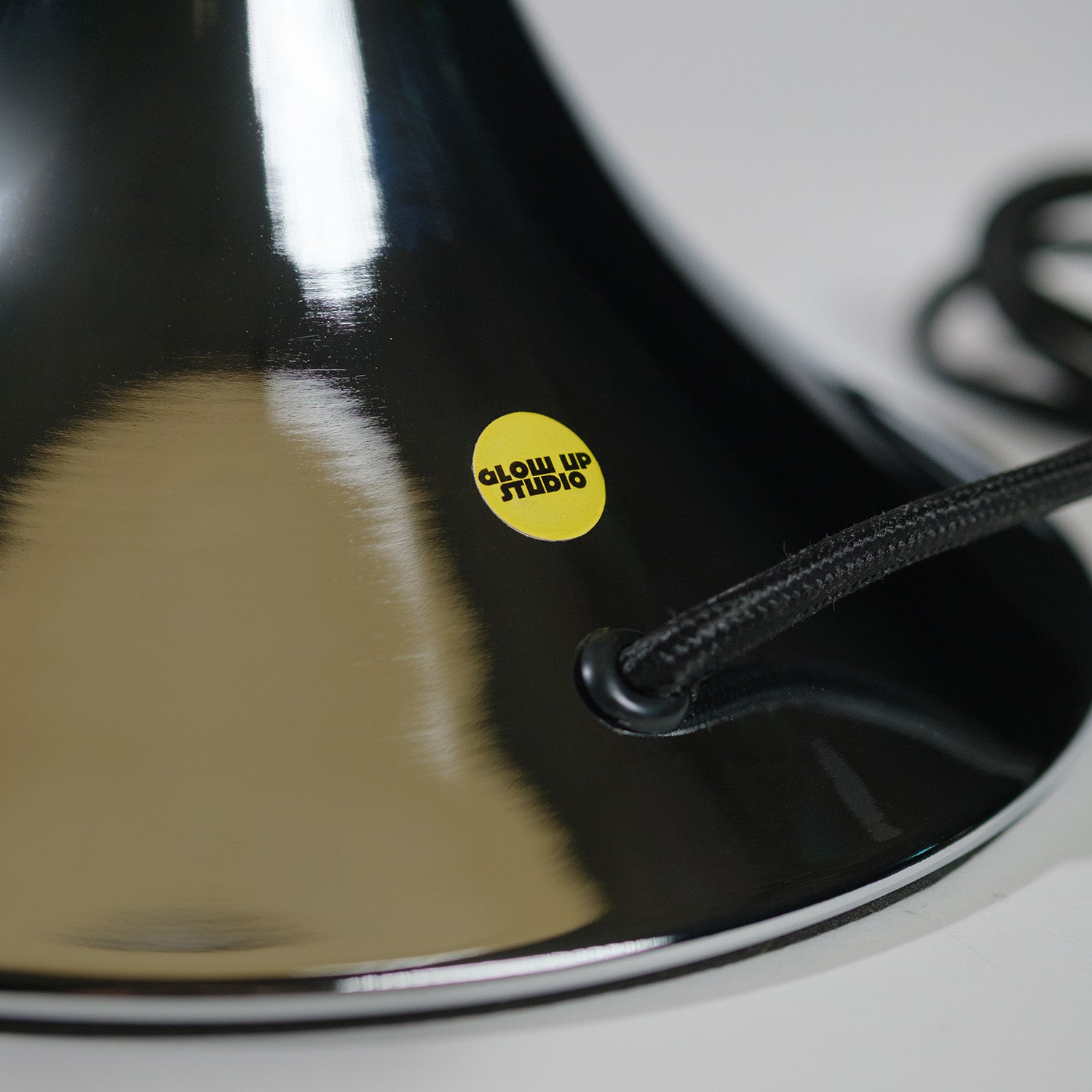 Nahaufnahme der verchromten GLOW UP STUDIO Donut Lampe mit gelbem Markensticker und schwarzem Textilkabel. Der reflektierende Metall Oberfläche zeigt hochwertige Verarbeitung und modernes Design.