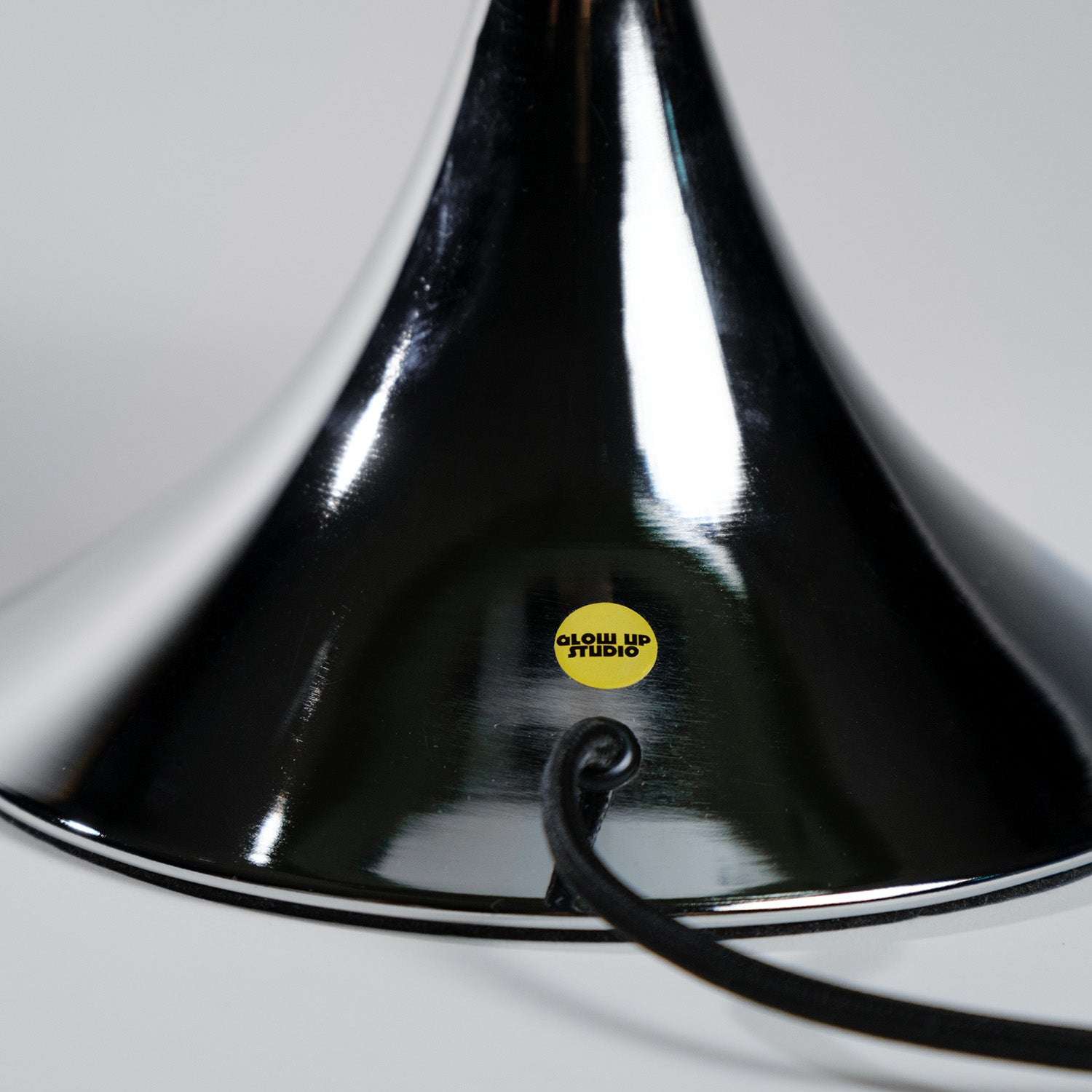 GLOW UP STUDIO Donut Lampe in glänzendem chrome, frontal fotografiert. Der gelbe Markensticker und das schwarze Kabel heben das minimalistische, hochwertige Lampendesign hervor.