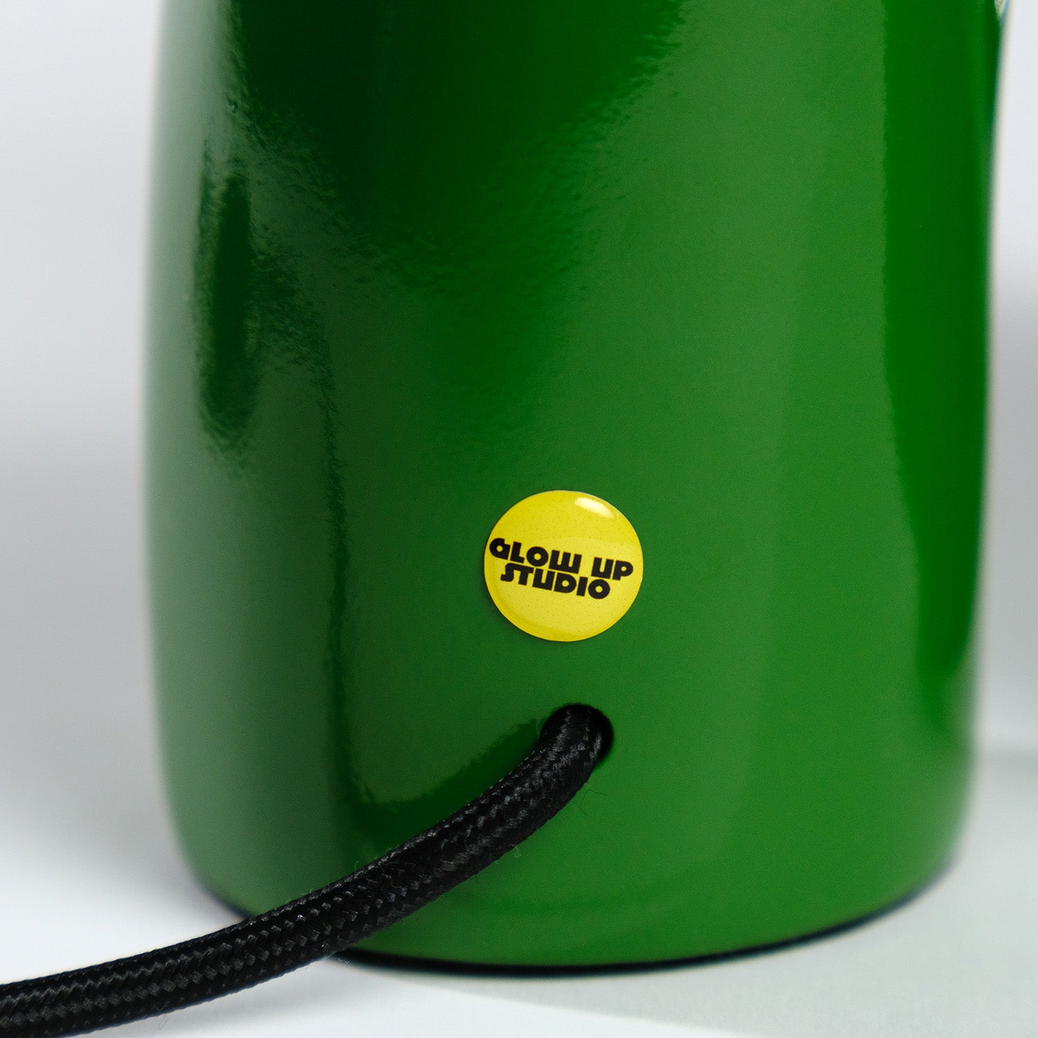 Detailaufnahme der grünen GLOW UP STUDIO Snake Lampe mit gelbem Markensticker. Das strukturierte Finish und das schwarze Textilkabel betonen die hochwertige Optik.