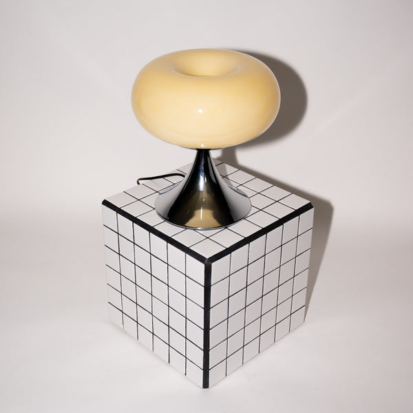 Moderne Nachttischlampe auf Designwürfel – Space Age Lampe mit glänzendem Chromfuß auf einem schwarz-weiß karierten Würfel. Die cremefarbene Leuchte verleiht dem minimalistischen Raum einen stilvollen 60er-Jahre-Touch.