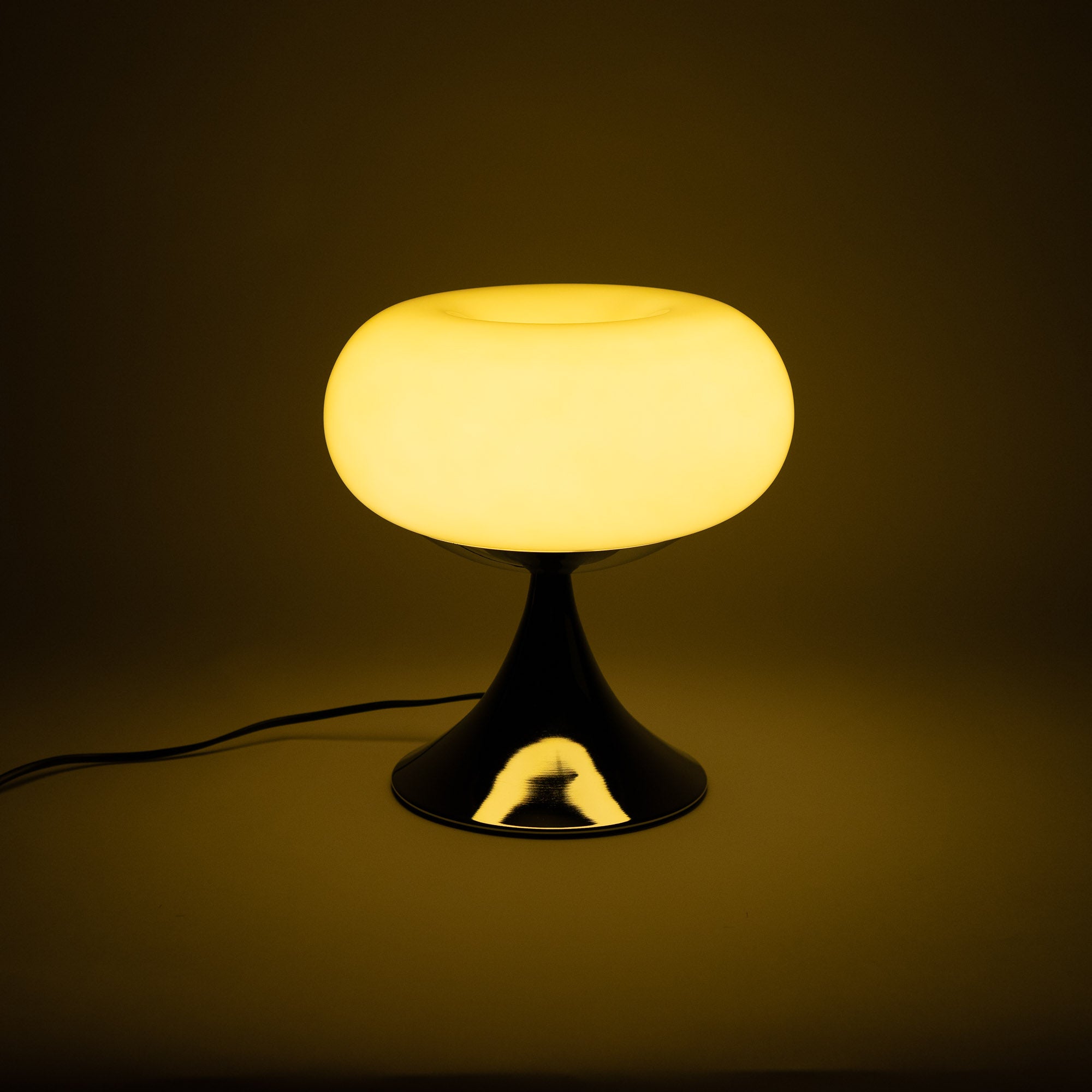 Die Lampe mit glänzendem Chromfuß strahlt warmes, diffuses Licht aus und schafft eine gemütliche Atmosphäre. Ihr ikonisches Mid-Century-Design erinnert an die 60er- und 70er-Jahre.