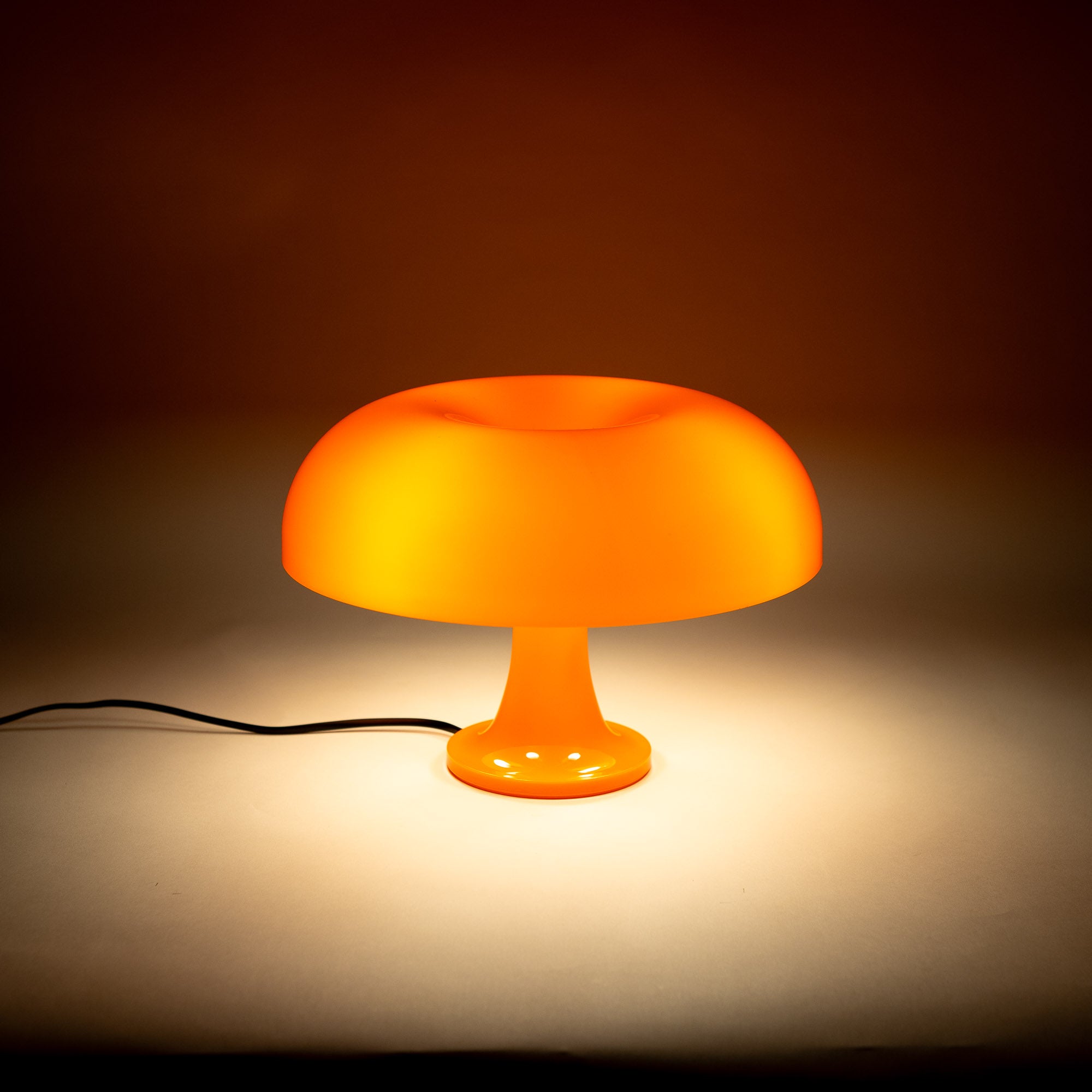 Die eingeschaltete orange Pilzlampe verbreitet weiches Licht auf einer neutralen Fläche. Ihr sanftes Leuchten sorgt für eine gemütliche Atmosphäre, ideal als stilvolles Nachtlicht oder dekorative Akzentbeleuchtung.