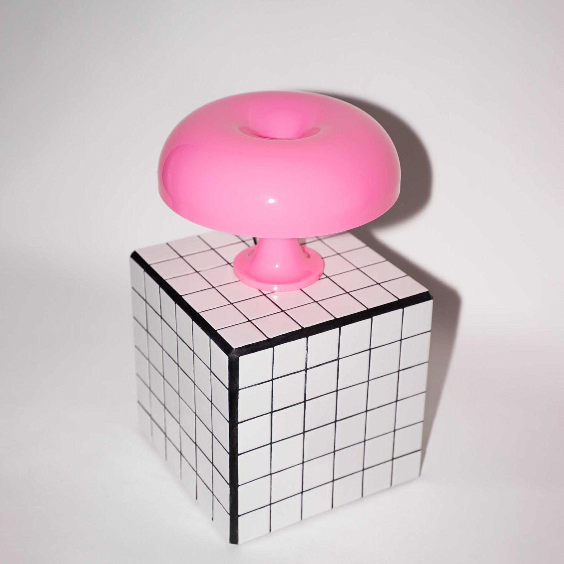 Die rosa Pilzlampe steht auf einem schwarz-weiß karierten Beistelltisch. Die Kombination aus geometrischem Muster und organischer Lampenform schafft ein modernes, stilvolles Ambiente.