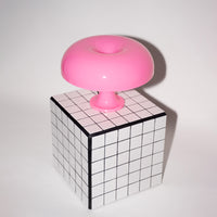 Die rosa Pilzlampe steht auf einem schwarz-weiß karierten Beistelltisch. Die Kombination aus geometrischem Muster und organischer Lampenform schafft ein modernes, stilvolles Ambiente.