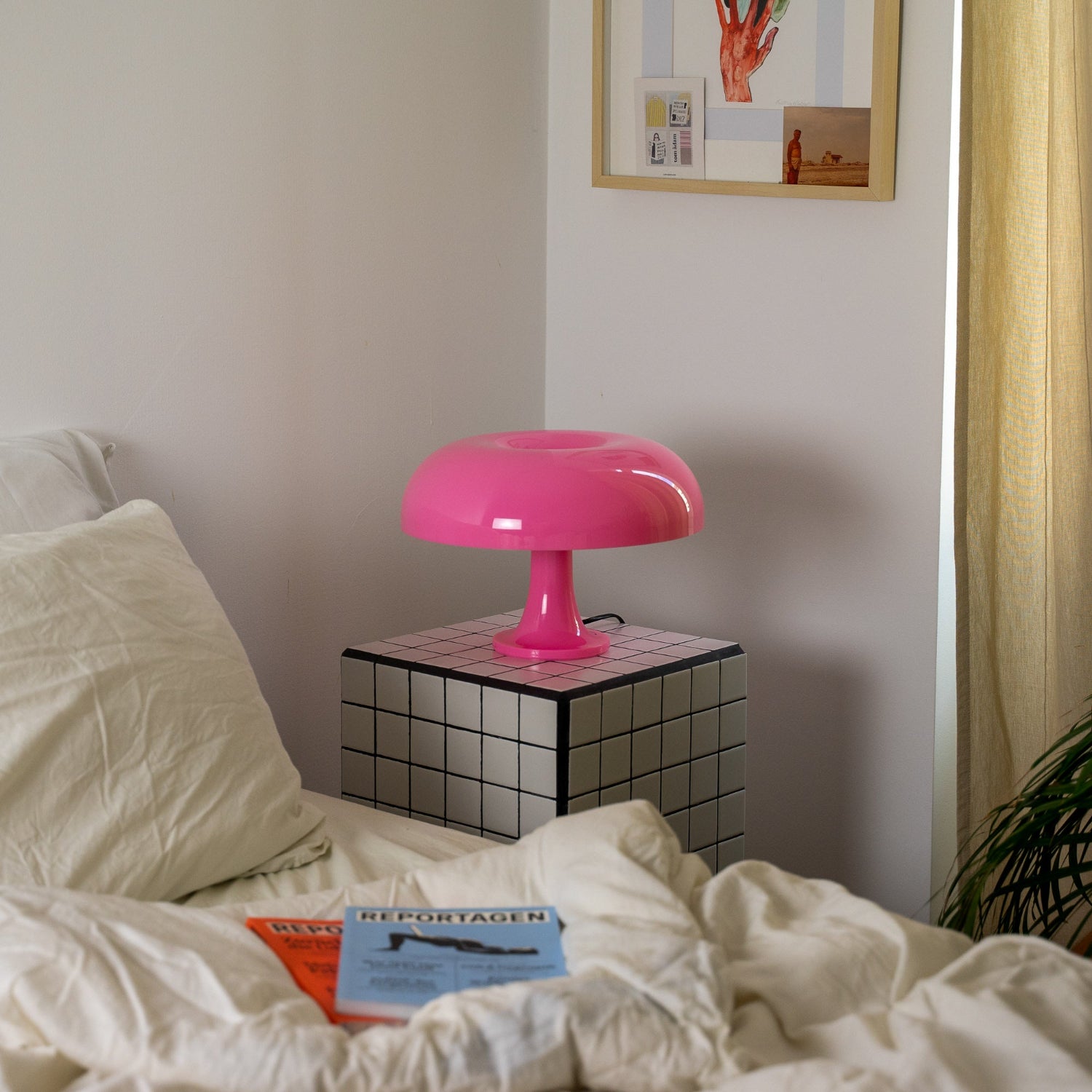 Die Designerlampe steht auf einem modernen, schwarz-weiß karierten Nachttisch neben einem Bett mit weißer Bettwäsche. Ihr weiches Licht schafft eine warme Atmosphäre für entspannte Abende.