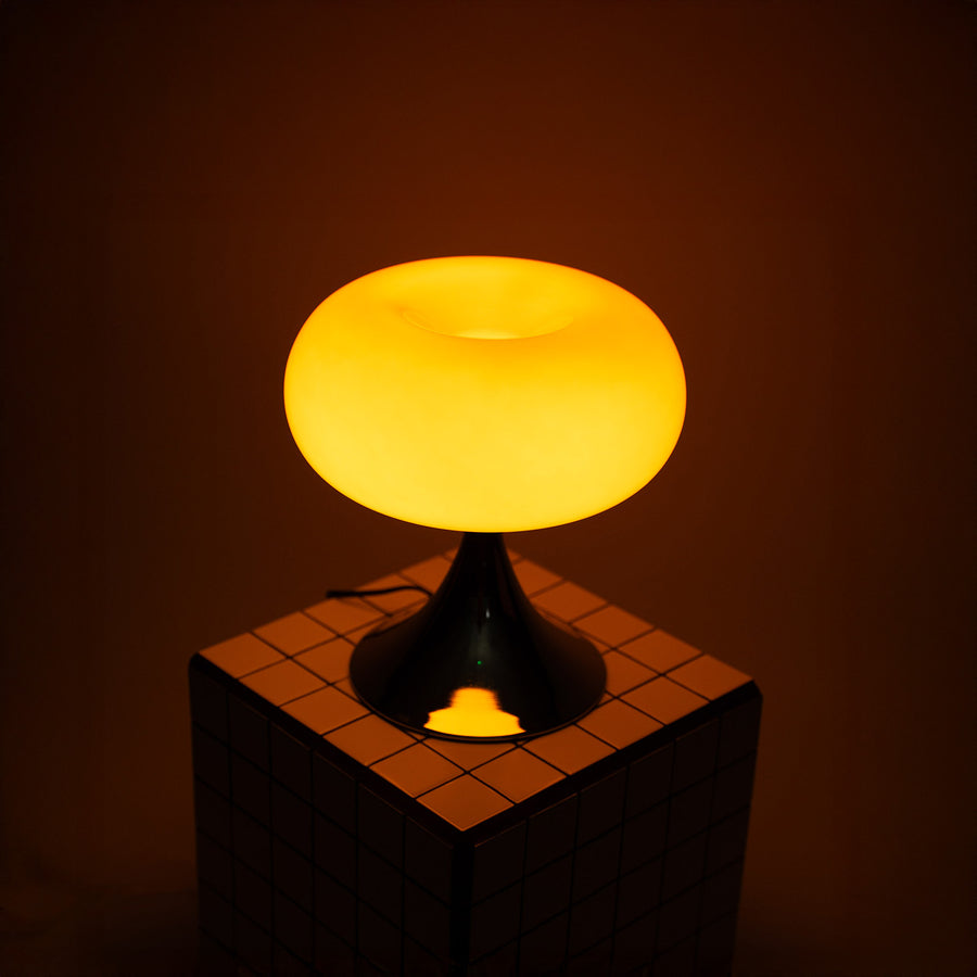 Die eingeschaltete orange Donut Lampe verbreitet weiches Licht auf einer neutralen Fläche. Ihr sanftes Leuchten sorgt für eine gemütliche Atmosphäre, ideal als stilvolles Nachtlicht oder dekorative Akzentbeleuchtung.