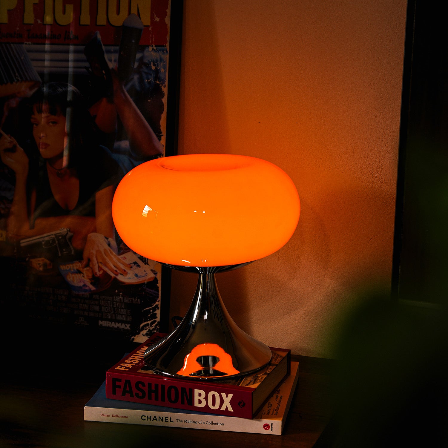 Orange Retro Tischlampe von GLOW UP STUDIO – Mid Century Lampe mit Chromfuß sorgt für warmes Licht im Wohnzimmer mit Pulp Fiction Poster im Hintergrund.
