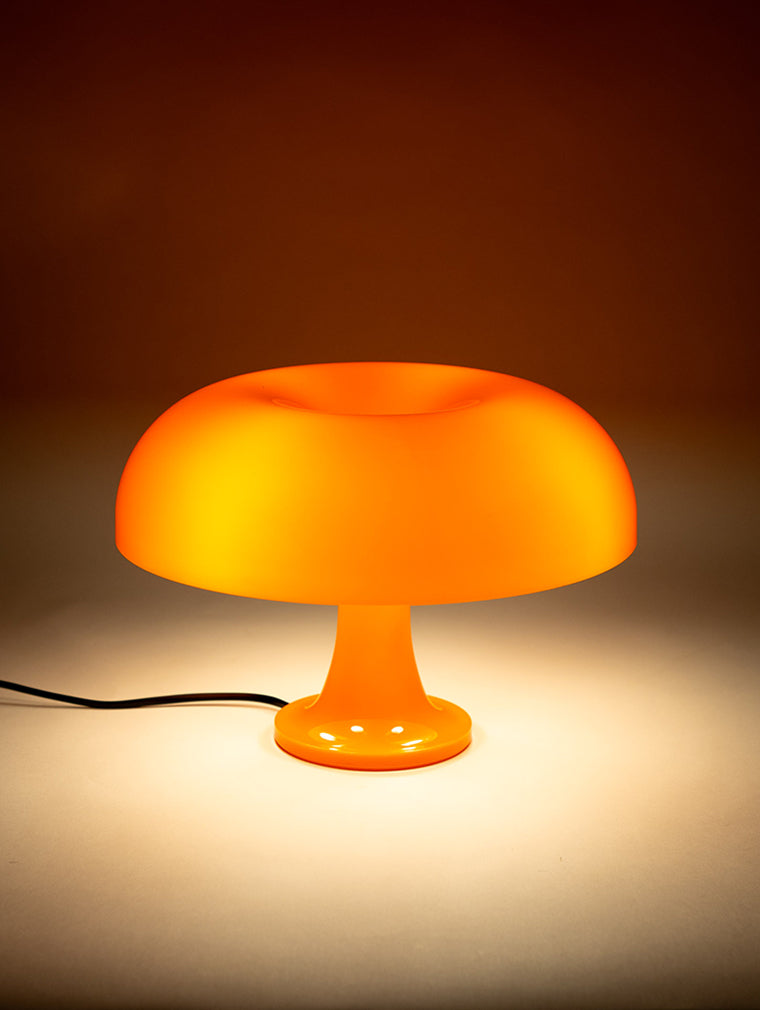 Die eingeschaltete orange Pilzlampe verbreitet weiches Licht auf einer neutralen Fläche. Ihr sanftes Leuchten sorgt für eine gemütliche Atmosphäre, ideal als stilvolles Nachtlicht oder dekorative Akzentbeleuchtung.