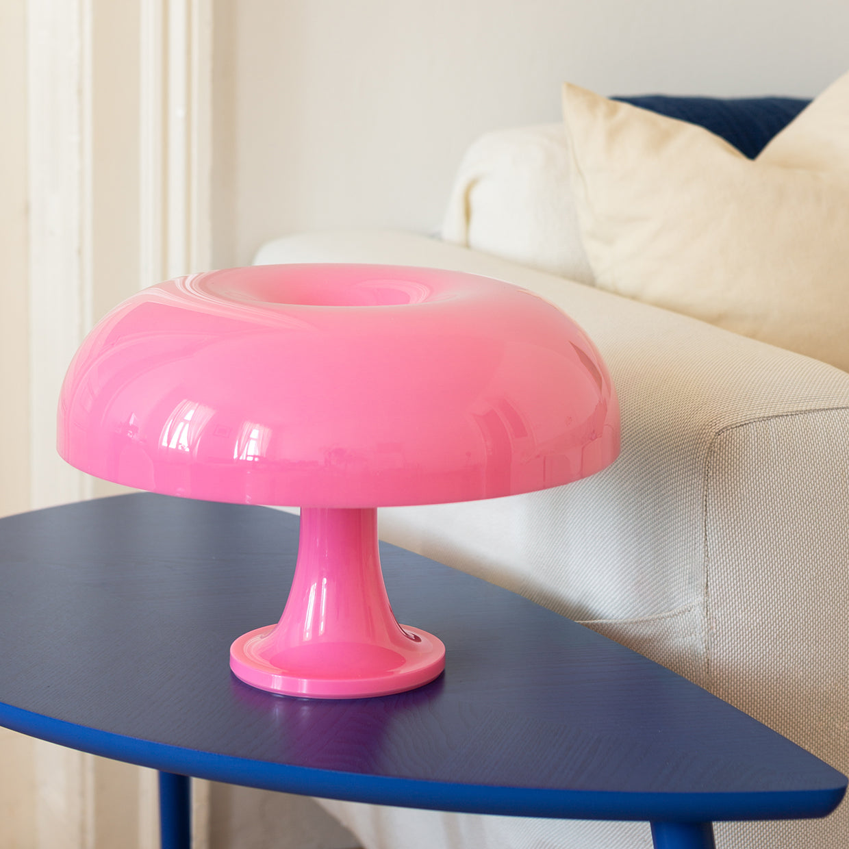 Die pinke Pilzlampe ergänzt das minimalistische Interieur mit ihrem kräftigen Farbton. Der Kontrast zwischen glänzendem Rosa und dem tiefblauen Tisch verleiht dem Raum eine besondere Dynamik.