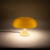 Die cremefarbene Pilzlampe mit glänzendem Acrylschirm und geschwungener Form steht auf einer weißen Oberfläche vor neutralem Hintergrund. Das hochwertige Material und die ikonische Form machen sie zu einem Designklassiker.