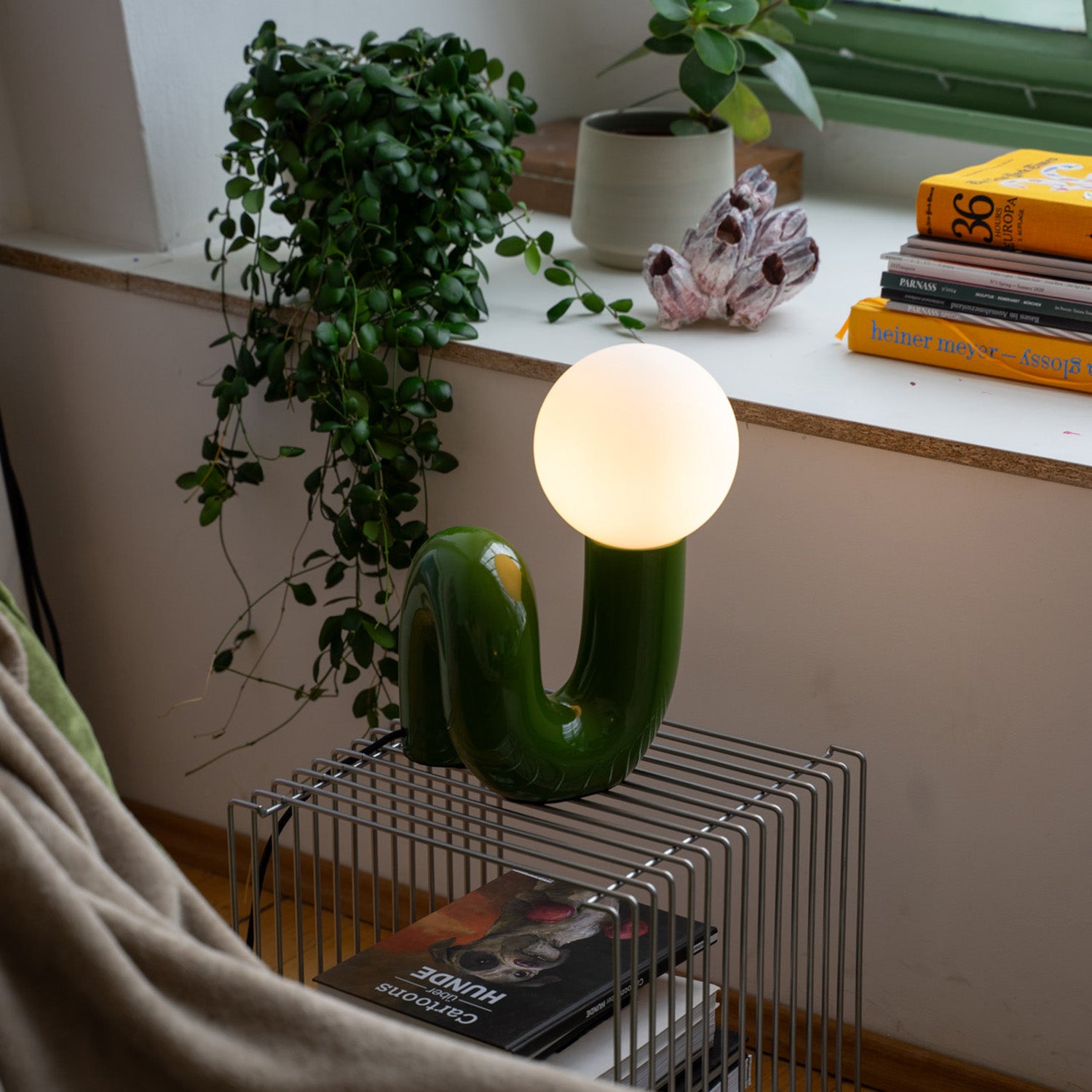 Retro Tischlampe Snake in Grün von GLOW UP STUDIO – organische Lampe mit Kugel-Leuchtkopf auf modernem Metalltisch, gemütliches Wohnzimmer mit Pflanzen und Büchern.