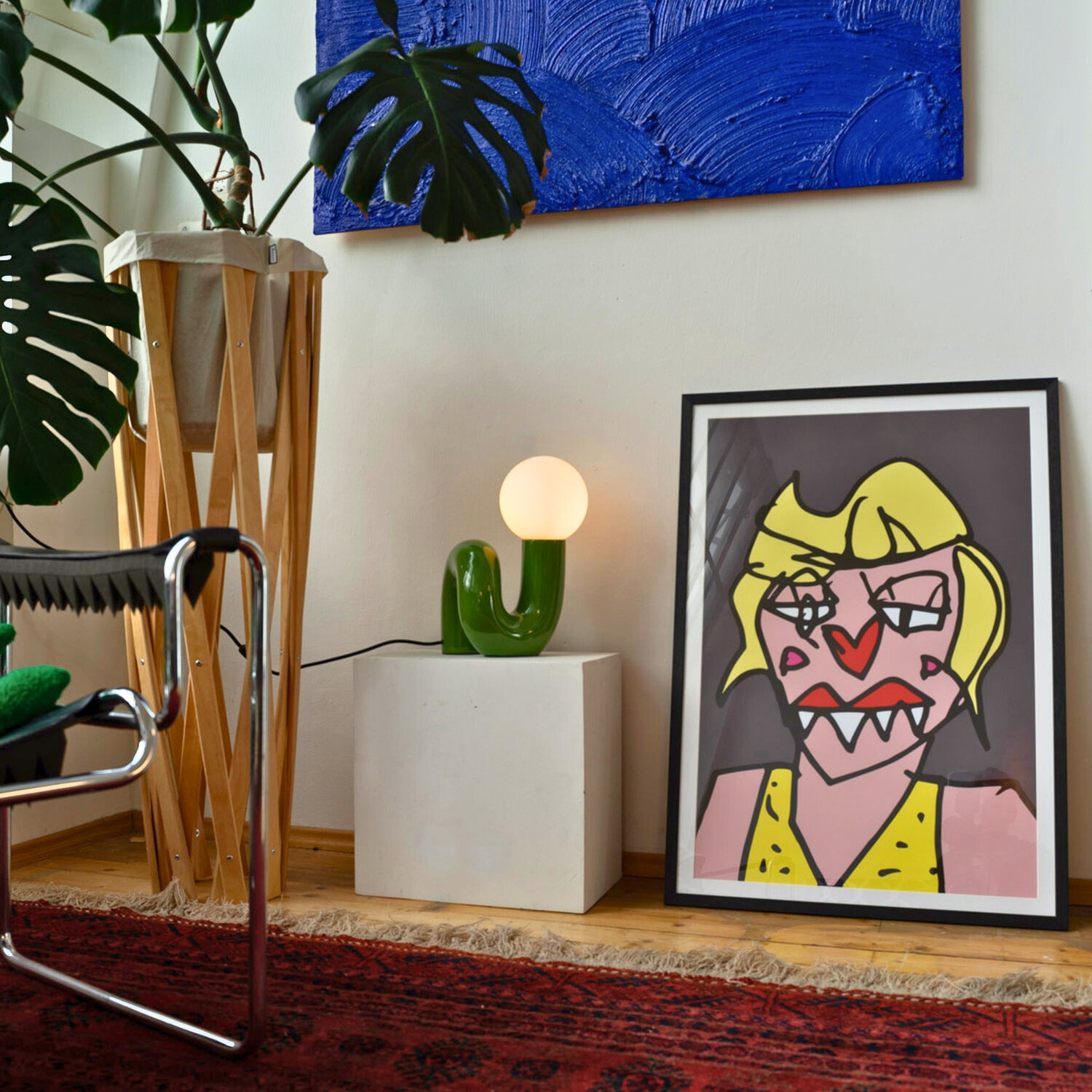 Retro Tischlampe Snake in Grün von GLOW UP STUDIO – organische Lampe mit Kugel-Leuchtkopf auf Podest, modernes Wohnzimmer mit Kunst, Pflanzen und Teppich.