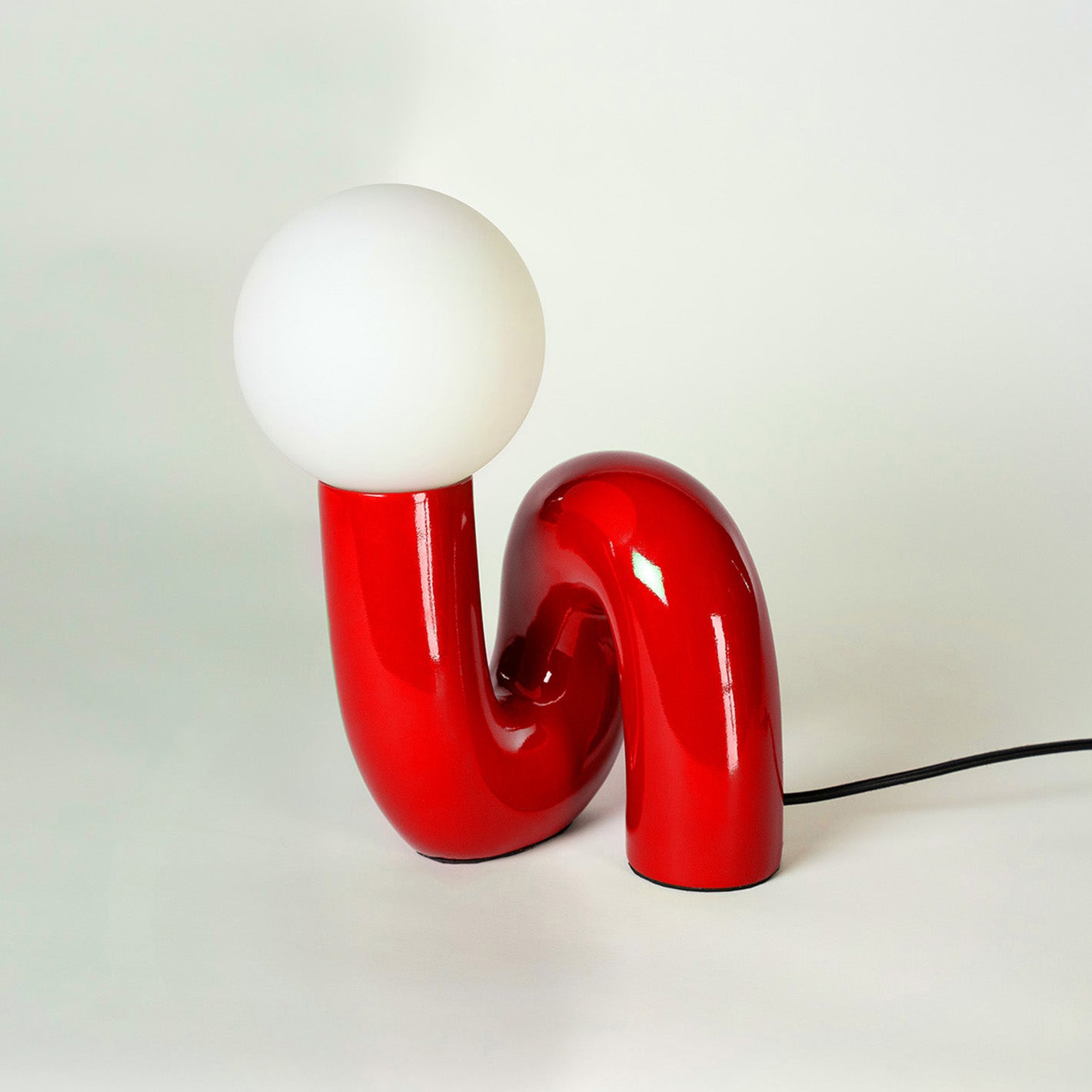 Design-Tischlampe in glänzendem Rot mit geschwungener, U-förmiger Basis und opalweißer Kugel als Leuchtkörper. Die skulpturale Lampe im Midcentury-Style setzt einen modernen, verspielten Akzent.