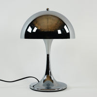 Verchromte Midcentury-Tischlampe mit halbrundem Schirm und elegant geschwungenem Standfuß auf weißem Hintergrund. Der glänzende Schirm spiegelt den Raum und erzeugt einen minimalistischen, modernen Look.