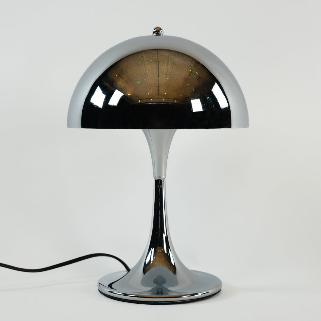 Verchromte Midcentury-Tischlampe mit halbrundem Schirm und elegant geschwungenem Standfuß auf weißem Hintergrund. Der glänzende Schirm spiegelt den Raum und erzeugt einen minimalistischen, modernen Look.