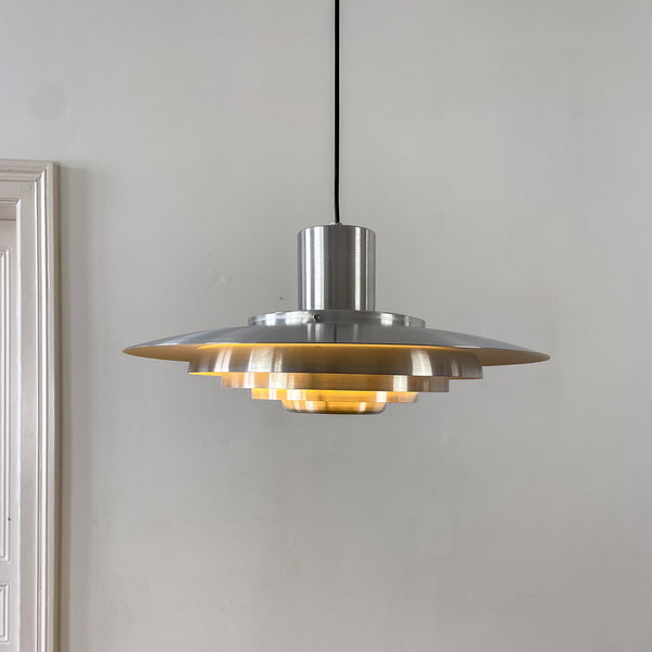Chromlampe mit gestuftem Reflektorschirm, ideal für Esszimmer oder Büros. Der Hintergrund mit weißen Wänden und einer klassischen Altbau-Tür unterstreicht das reduzierte Design.