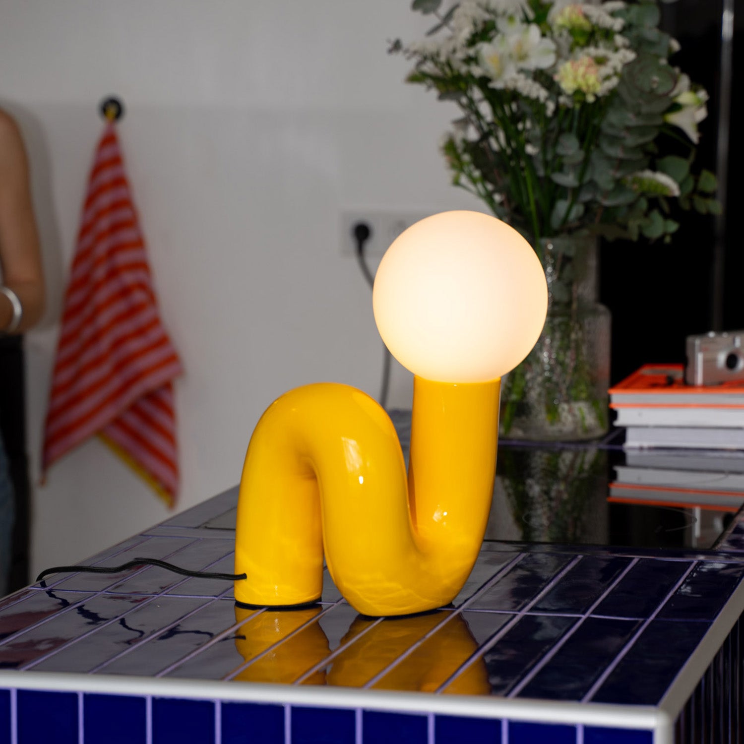 Snake Lampe Gelb mit runder Glaskugel als 60s Retro Tischlampe auf blauem Fliesentisch in modernem Interieur.