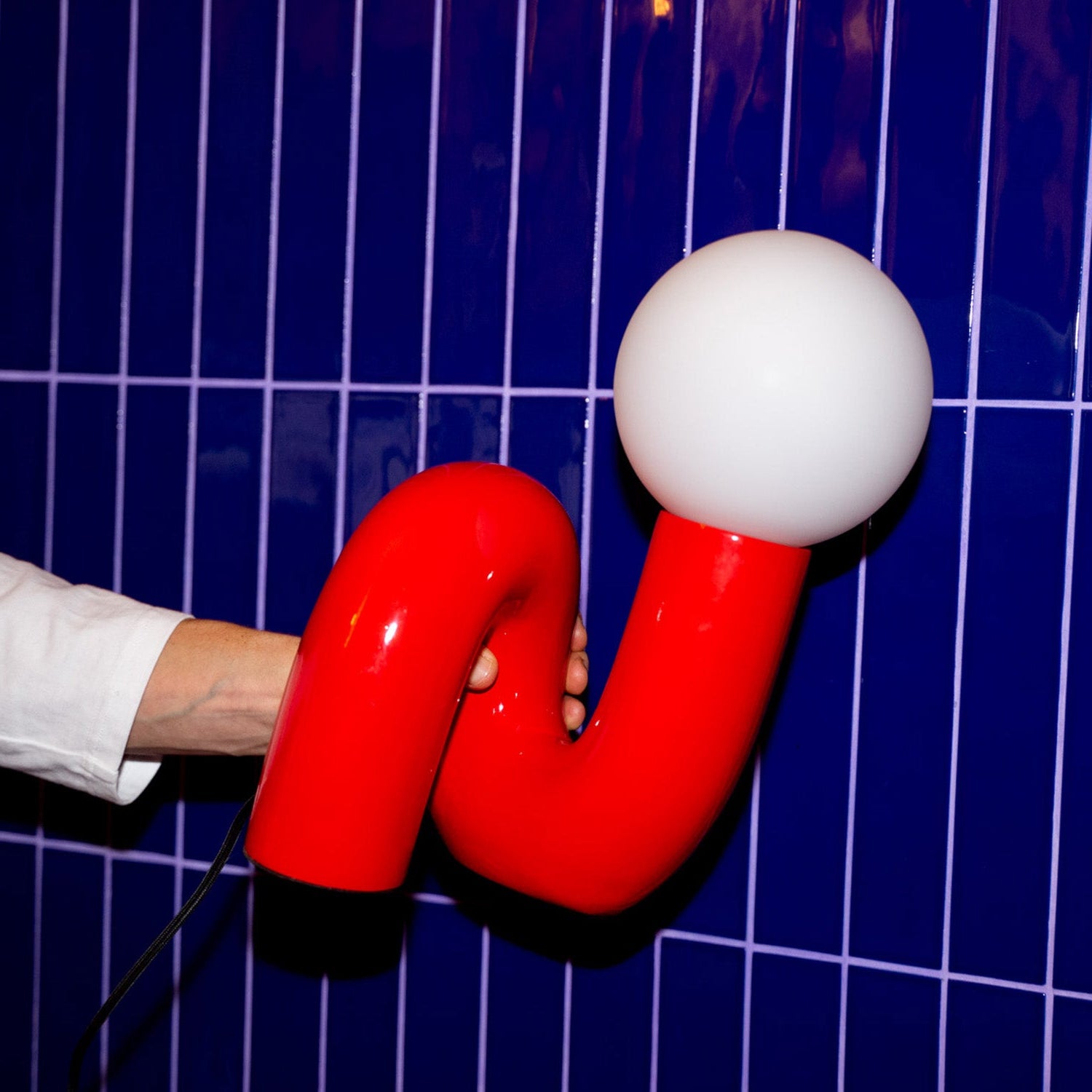 Rote Snake Lampe in der Hand gehalten vor blauer Fliesenwand, skulpturale Retro-Form mit runder Glaskugel