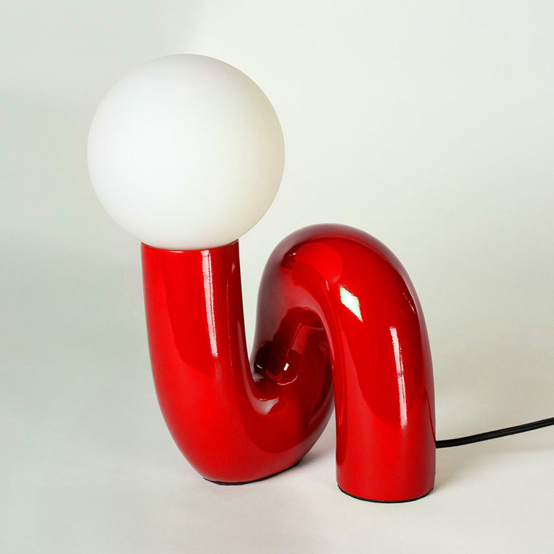 Rote Snake Design-Tischlampe mit glänzender Oberfläche und opalweißer Glaskugel vor weißem Studiohintergrund.